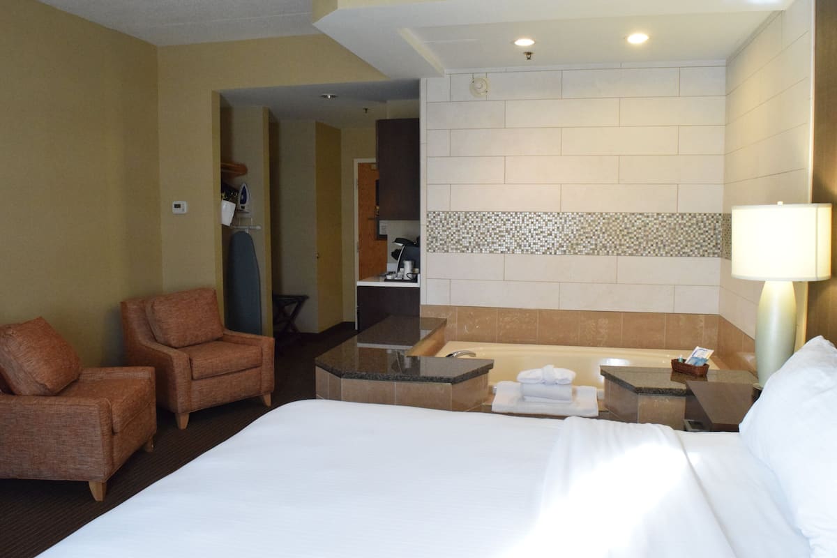 Habitación de hotel con cama, dos sillones, una pequeña zona de estar con mesa, bañera y espejo.