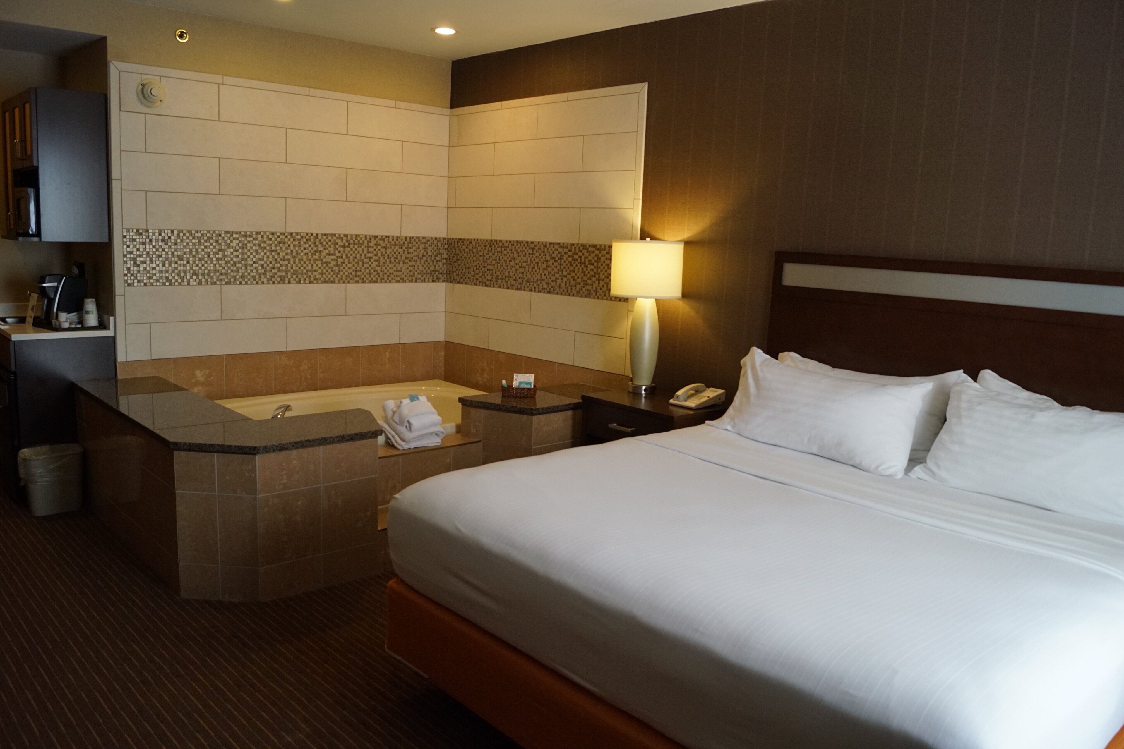 A hotel room with a bed, a bathroom with a bathtub, a desk with a telephone, and a coffee machine.
