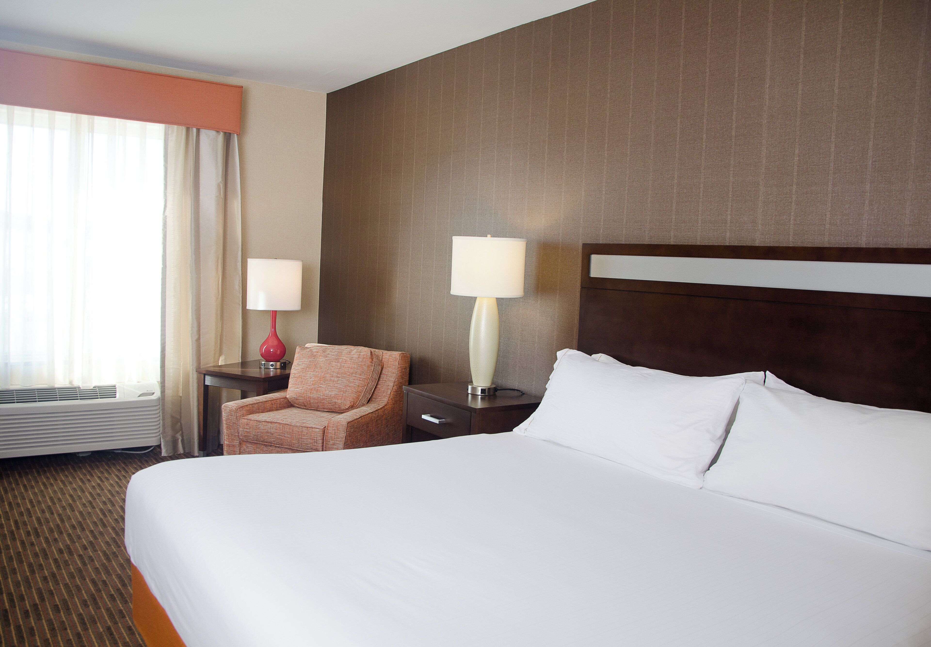 A hotel room with a large bed, a chair, two bedside tables, and a window with curtains.