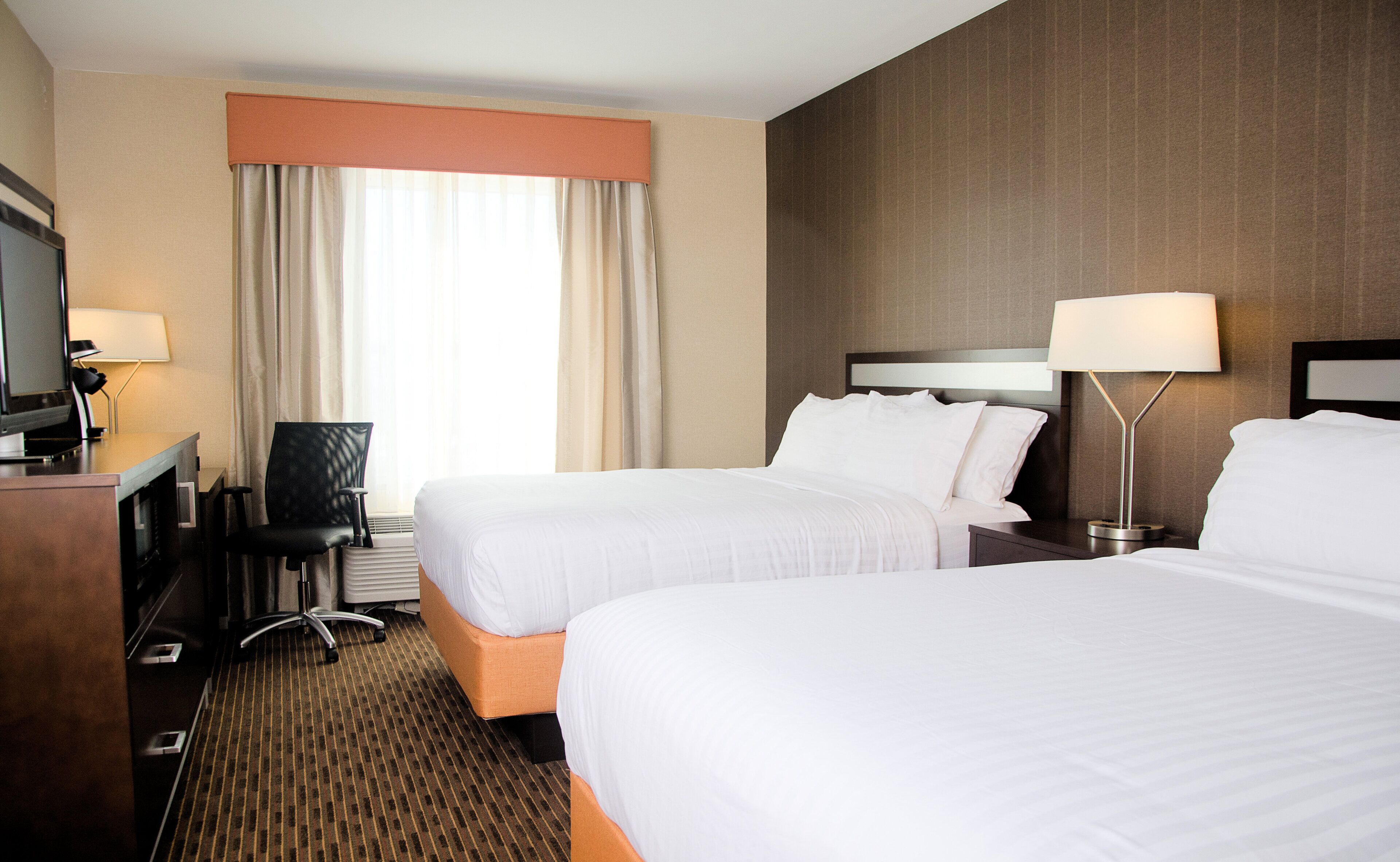A hotel room with two beds, a desk with a computer, a chair, and a TV.