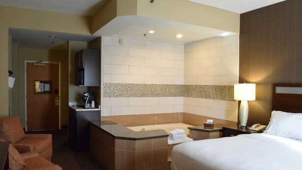 Une chambre d’hôtel comprenant un lit, un coin salon, une salle de bain avec baignoire et un bureau avec une lampe.