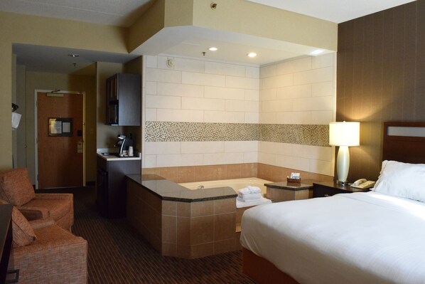 Habitación de hotel con cama, zona de estar, baño con bañera y escritorio con lámpara.
