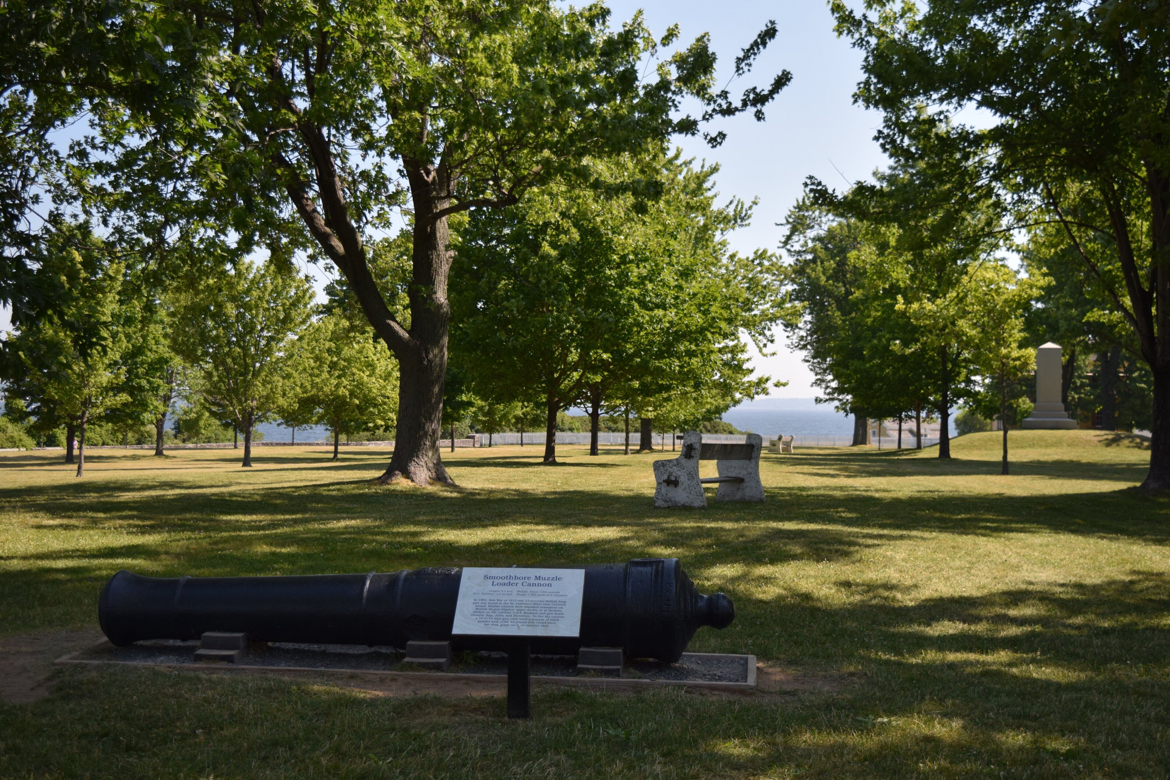 Un parco con un cannone storico esposto, circondato da alberi e una panchina.