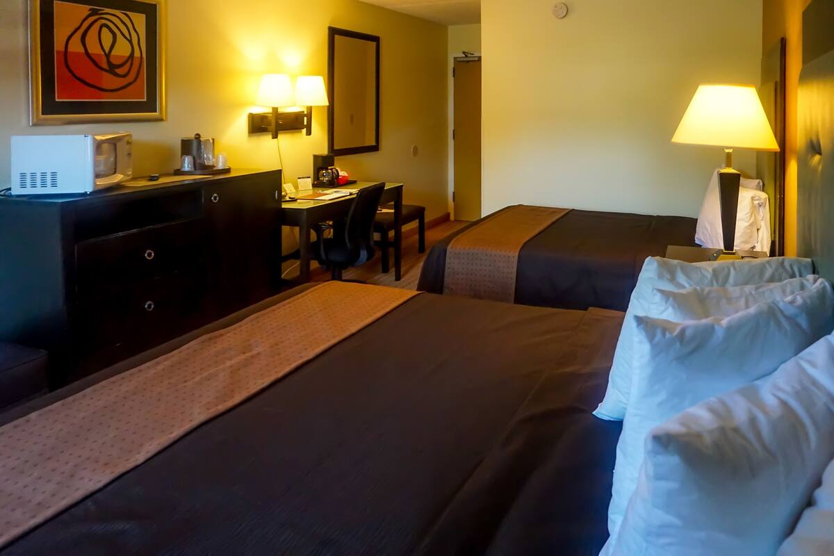 A hotel room with two beds, a desk with a chair, a microwave, and a lamp.