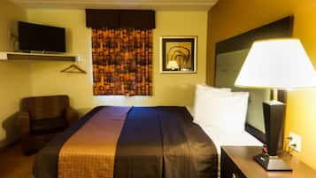A hotel room with a bed, a TV mounted on the wall, a lamp on a bedside table, and a chair.