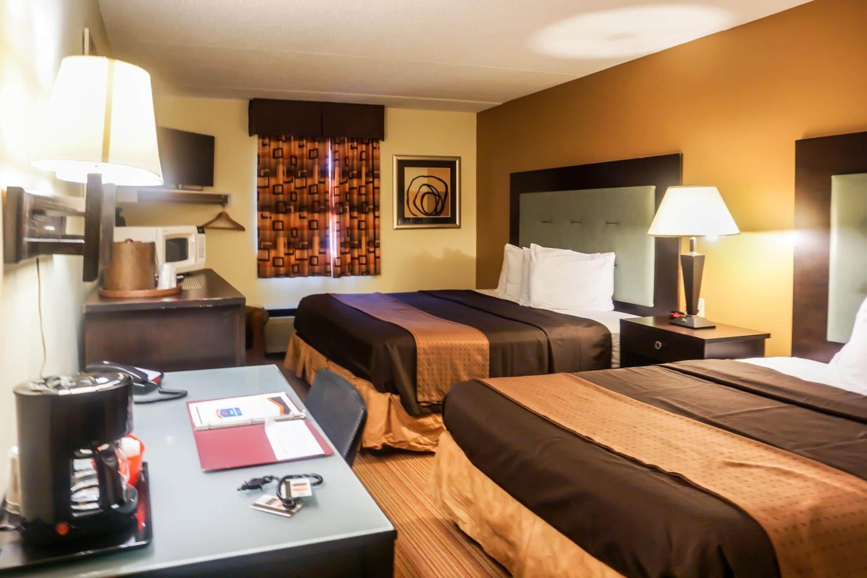 A hotel room with two beds, a desk with a coffee maker, a TV, and a microwave.