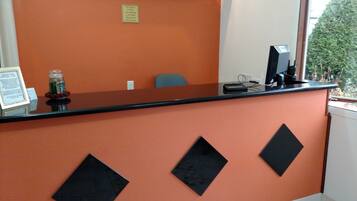 A reception desk with a black top and orange wall, a small sign indicating a non-smoking policy, and a chair in the background.