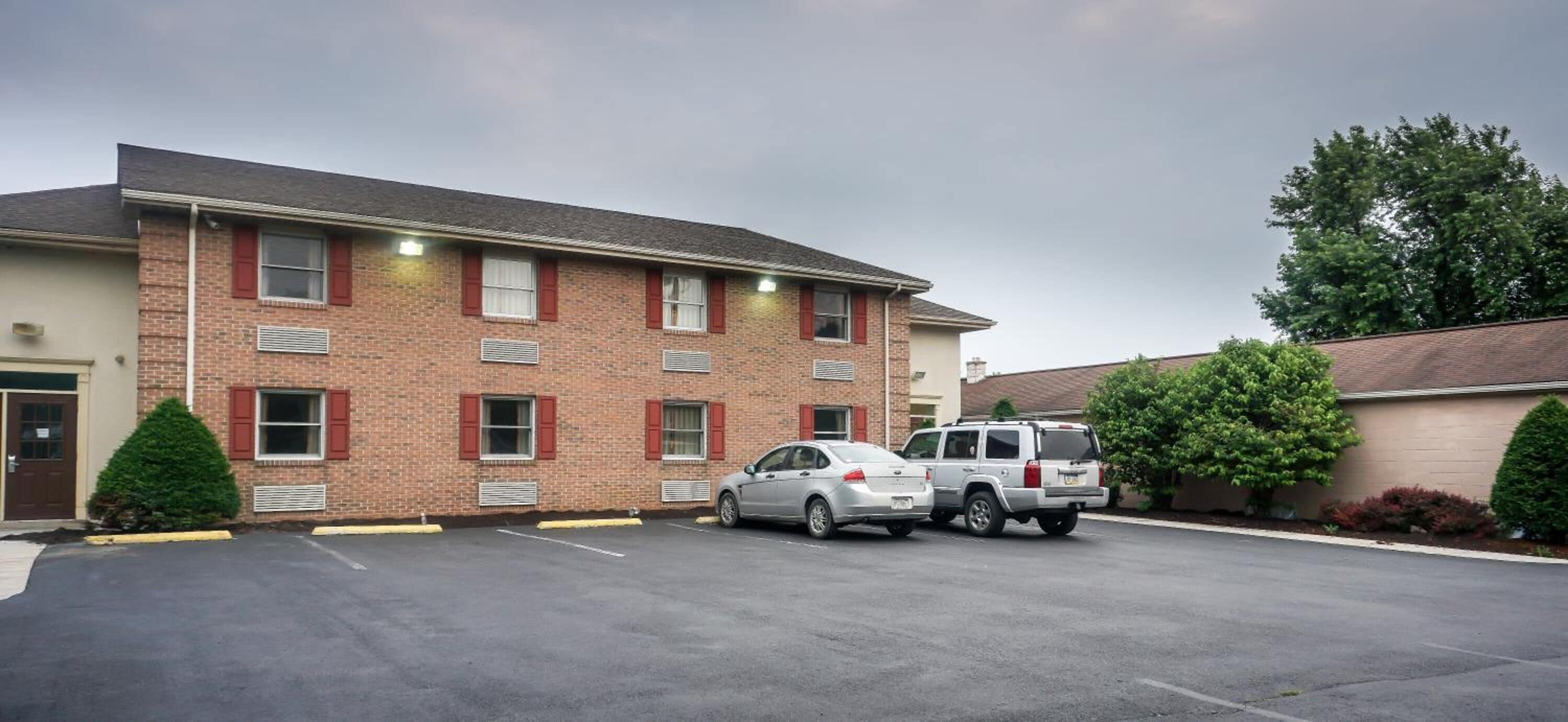 A two-story brick building with a parking lot. There are two cars parked in front.