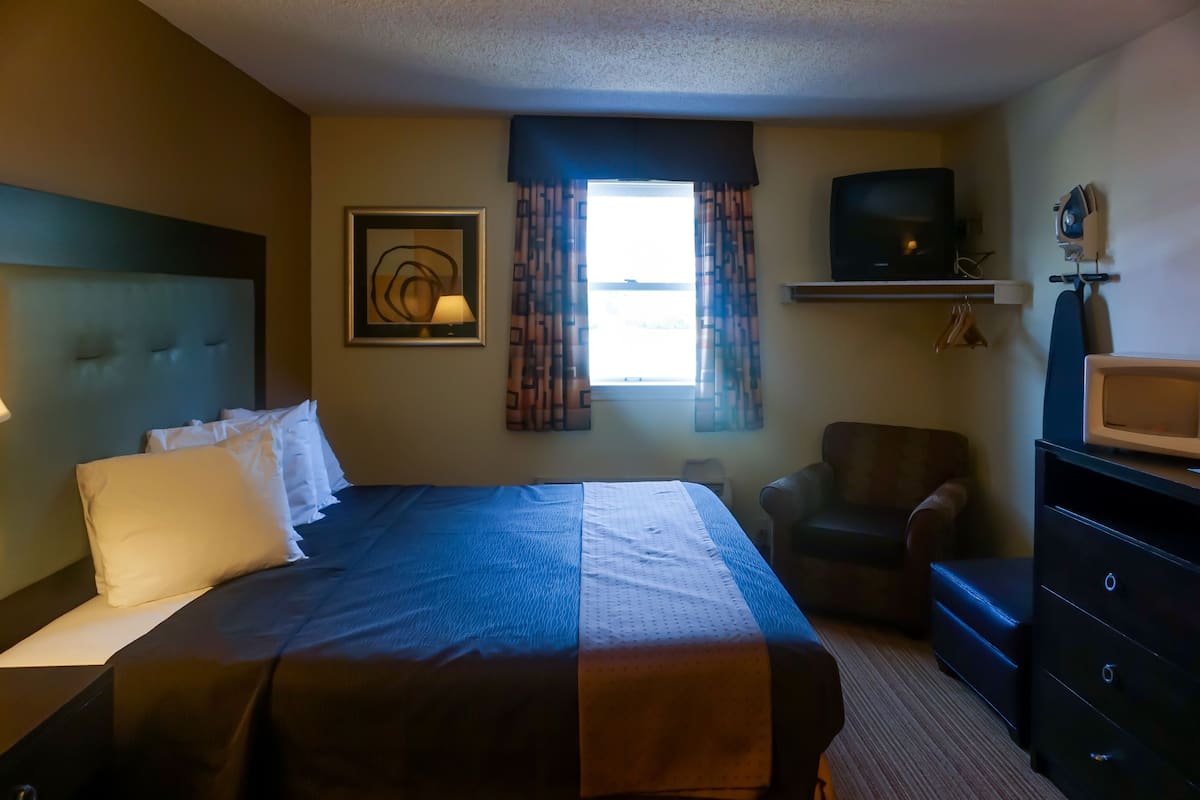 A hotel room with a large bed, a chair, a TV, and a dresser.