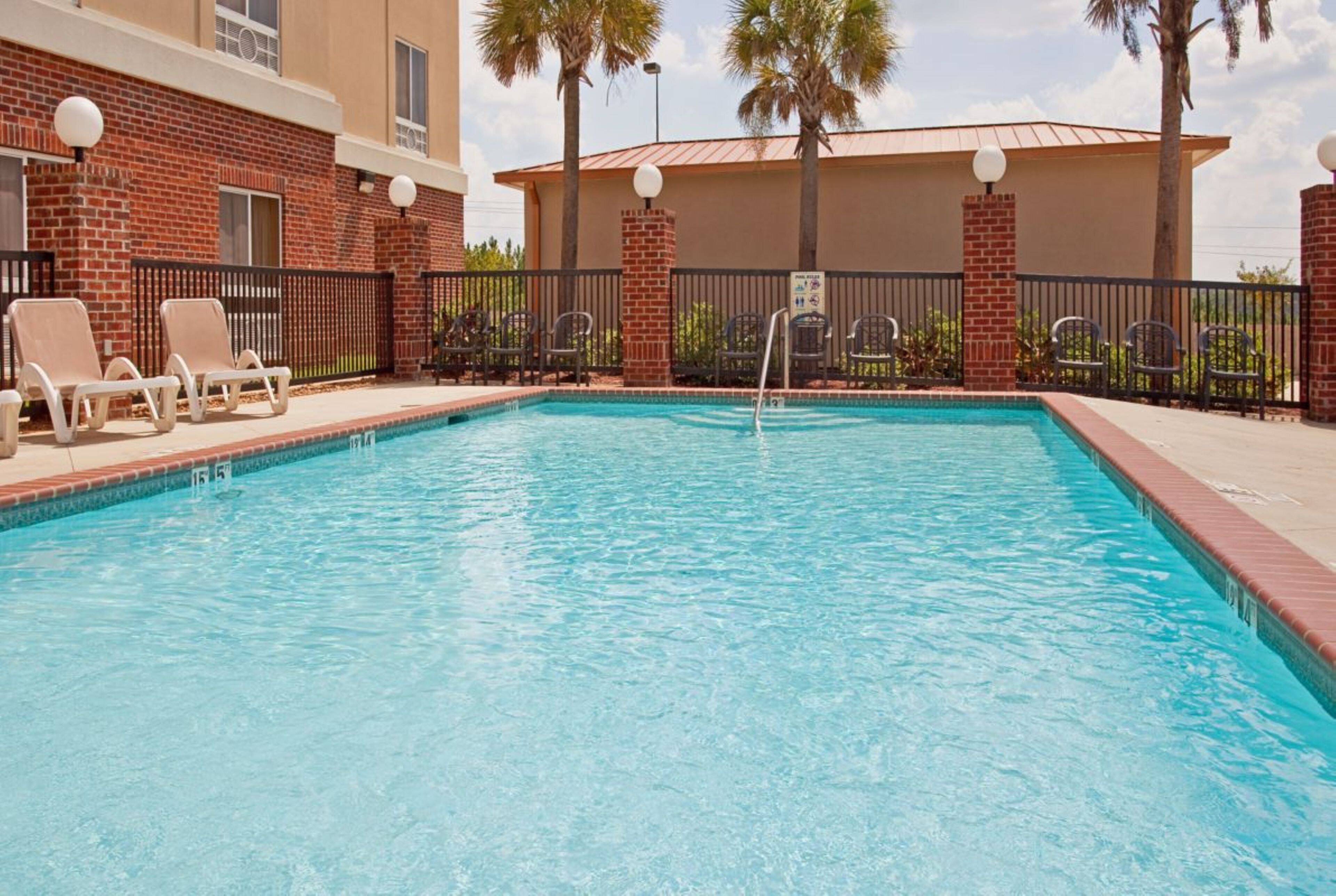 A rectangular swimming pool with a clear blue water surface, surrounded by a brick wall and a metal fence.