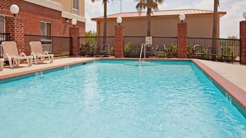 A rectangular swimming pool with a clear blue water surface, surrounded by a brick wall and a metal fence.