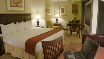 A hotel room with a bed, a desk with a laptop, a television, and a dining area with chairs and a table.