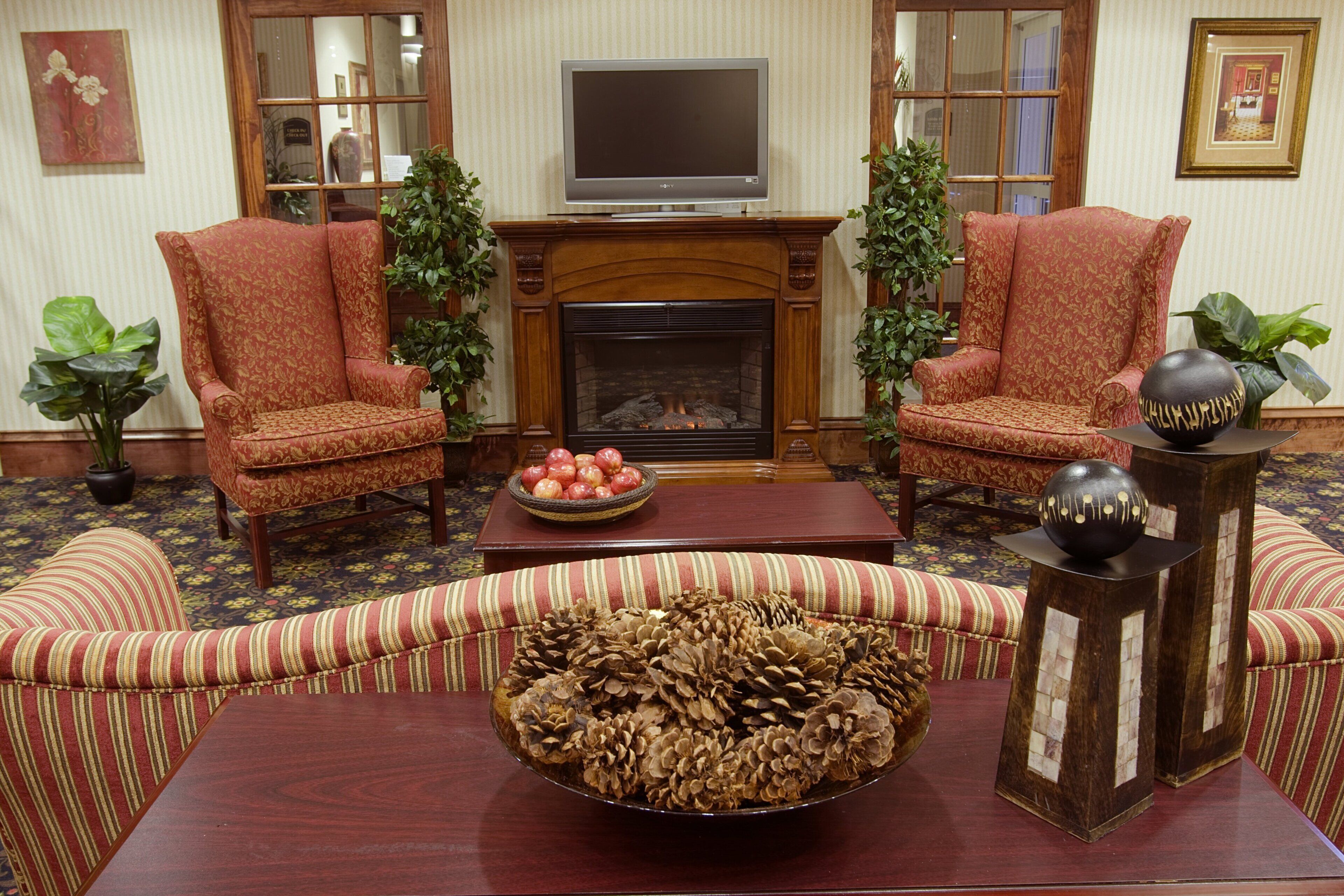 A living room with two armchairs, a sofa, a fireplace, a television, and a table with decorative items.