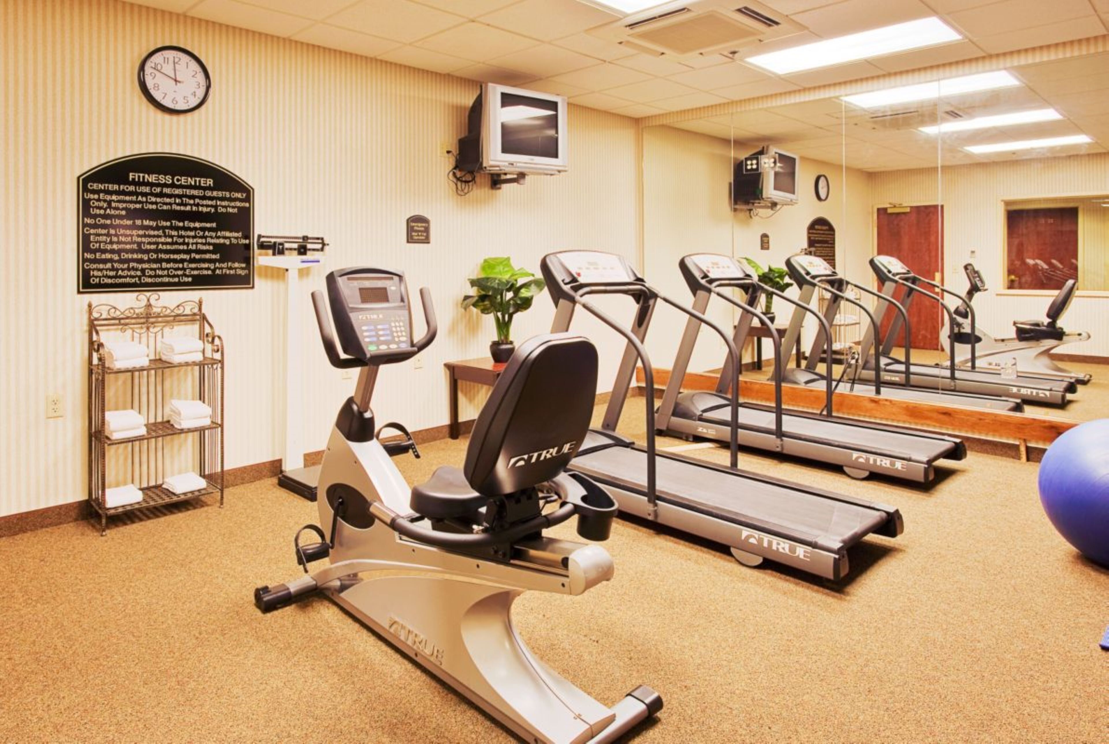 Un gimnasio con cintas de correr, elípticas y un reloj de pared.