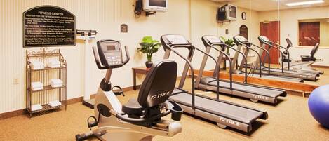 Un gimnasio con cintas de correr, elípticas y un reloj de pared.