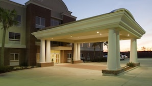 Entrada de hotel com alpendre coberto, fachada de tijolos e estacionamento.