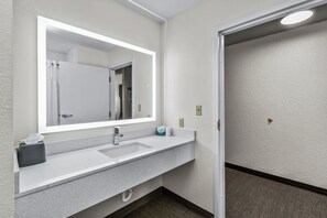 A bathroom with a white sink, a large mirror, and a towel dispenser.