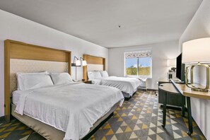A hotel room with two beds, a desk, a chair, a window with a view, and a lamp.