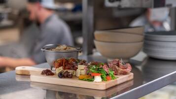 A wooden board with various food items, including meats, cheeses, and vegetables, on a stainless steel counter in a kitchen setting.