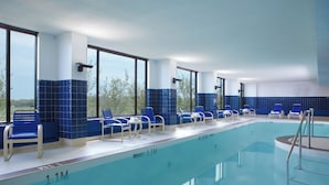Une piscine intérieure avec des chaises bleues et de grandes fenêtres.