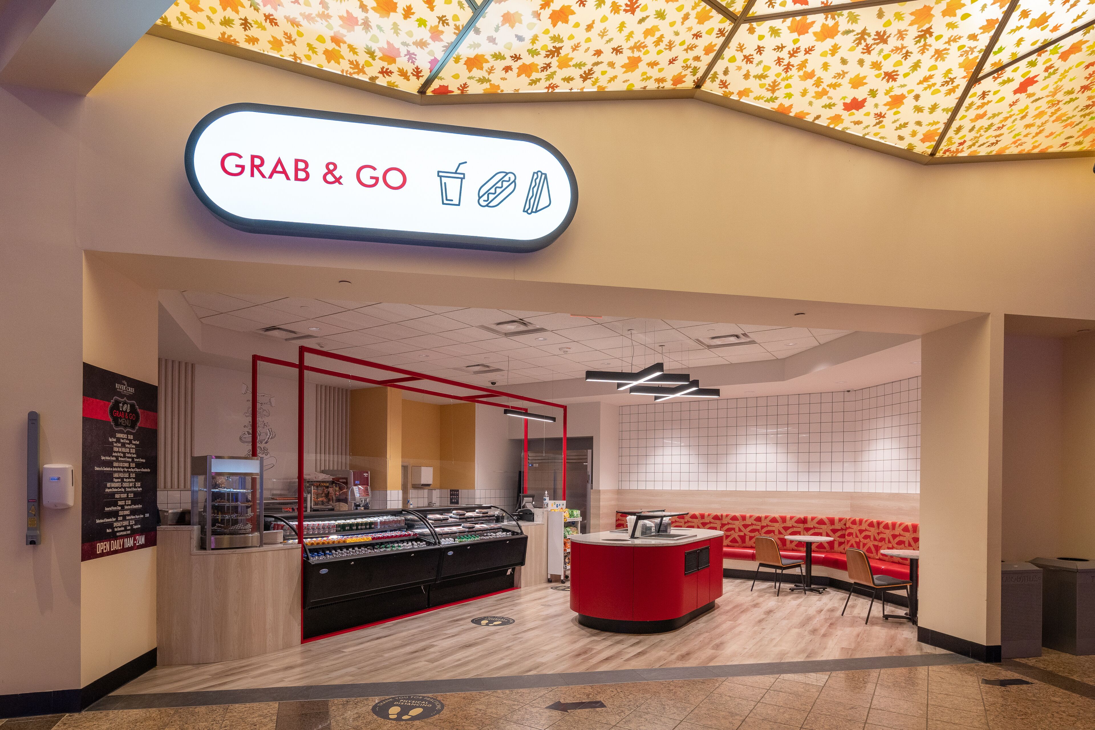 Un kiosque à nourriture moderne, avec une enseigne « à emporter », un comptoir doté d’un distributeur de boissons et un espace avec des banquettes rouges où l’on peut s’asseoir.