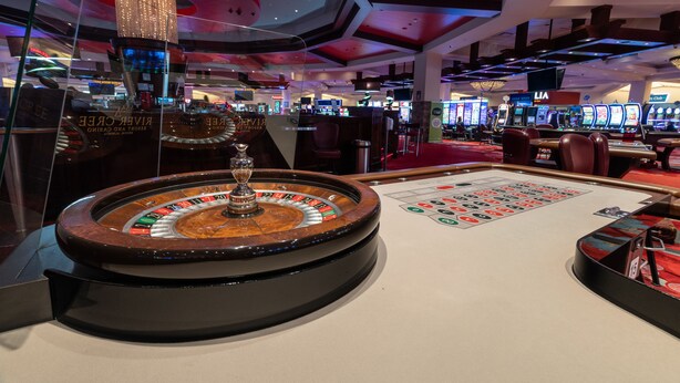 Une salle de casino avec une table de roulette, des machines à sous et un lustre.