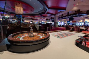 Een casino met roulette tafel, gokkasten en een kroonluchter.
