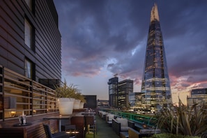 Eine Dachterrasse mit Sitzgelegenheiten im Freien, Blick auf den Stadtpanoramahimmel und moderne Architektur.
