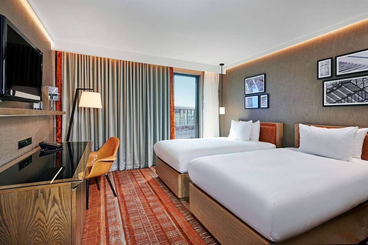 Habitación de hotel con dos camas, un escritorio, una silla, un televisor y una ventana con cortinas.