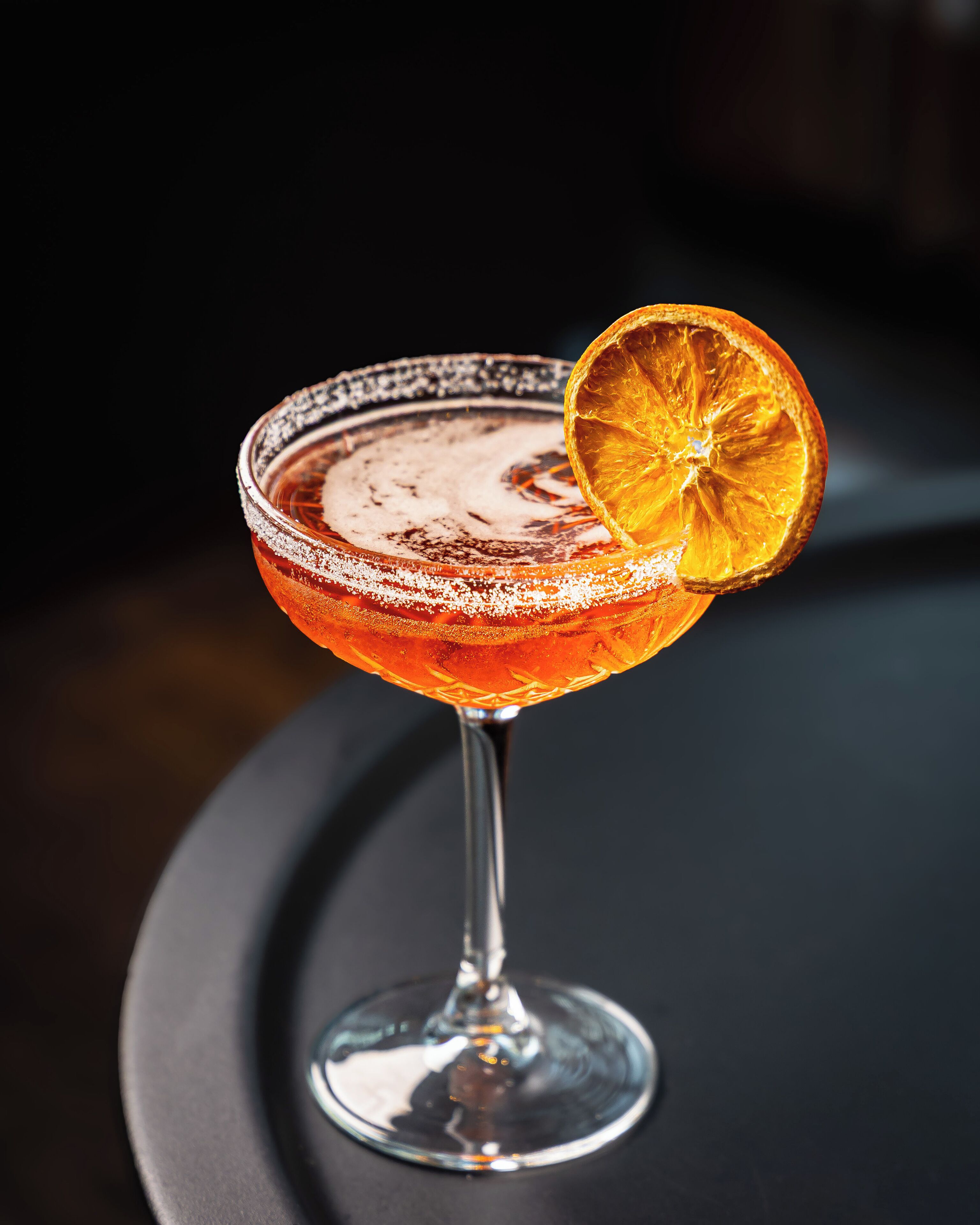 A cocktail in a glass with a salted rim and a dried orange slice garnish.
