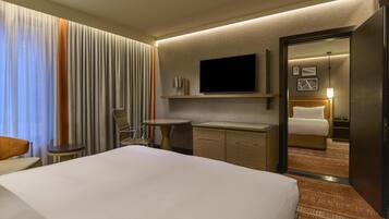 A hotel room with a large bed, a television mounted on the wall, a small round table, a cabinet, and a mirror reflecting the room.