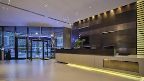 A modern hotel lobby with a revolving door, a reception desk, and a large window offering a view of the cityscape. - Hilton London Tower Bridge (London)