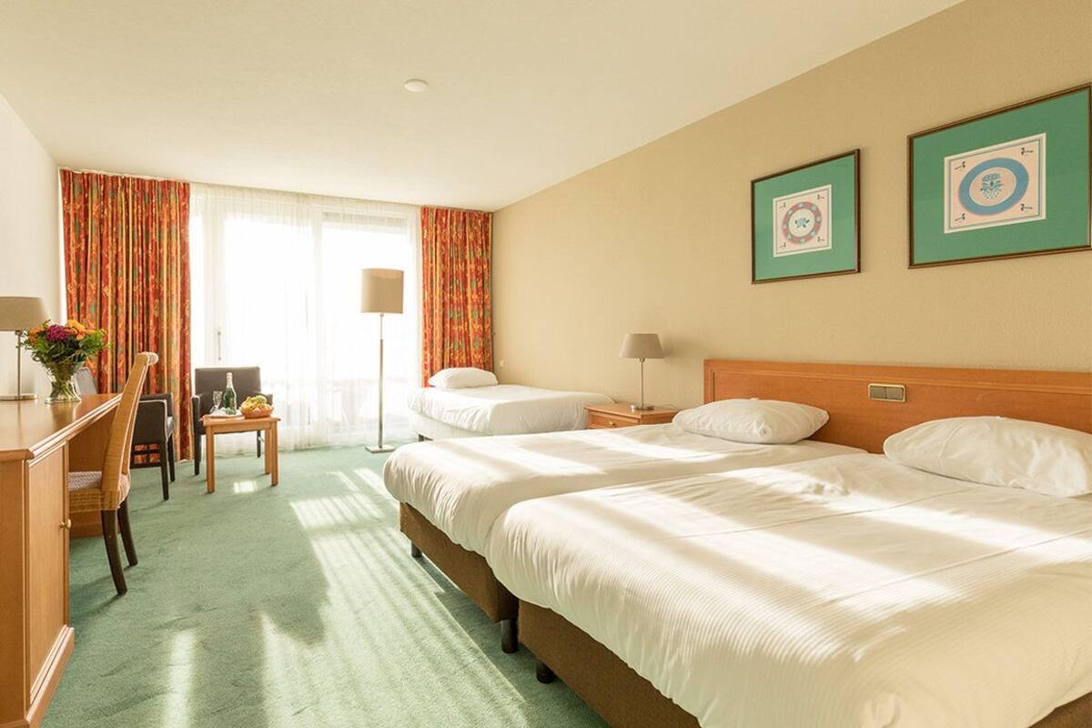 Ein Hotelzimmer mit zwei Betten, einem Schreibtisch, einem Stuhl und einem Tisch mit Blumen.