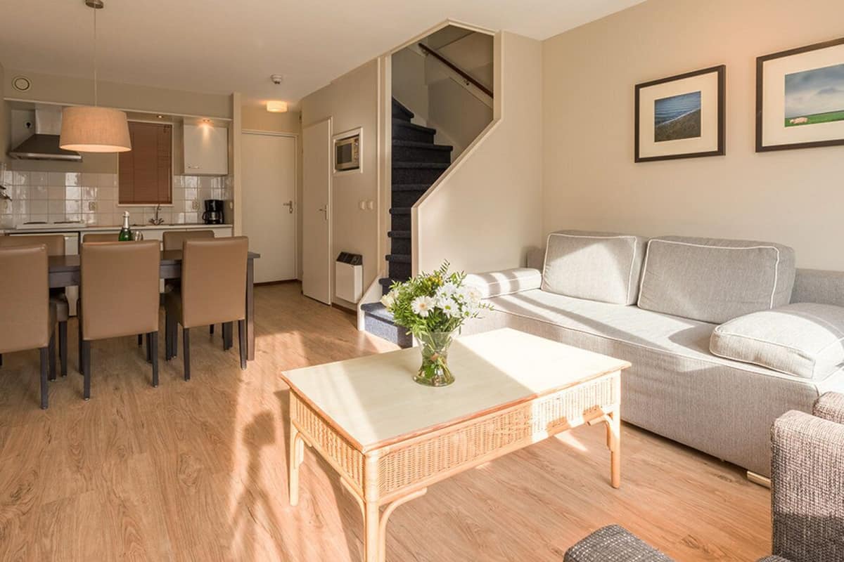 Ein modernes Wohnzimmer mit Sofa, Esstisch und Küchenbereich mit Treppe.