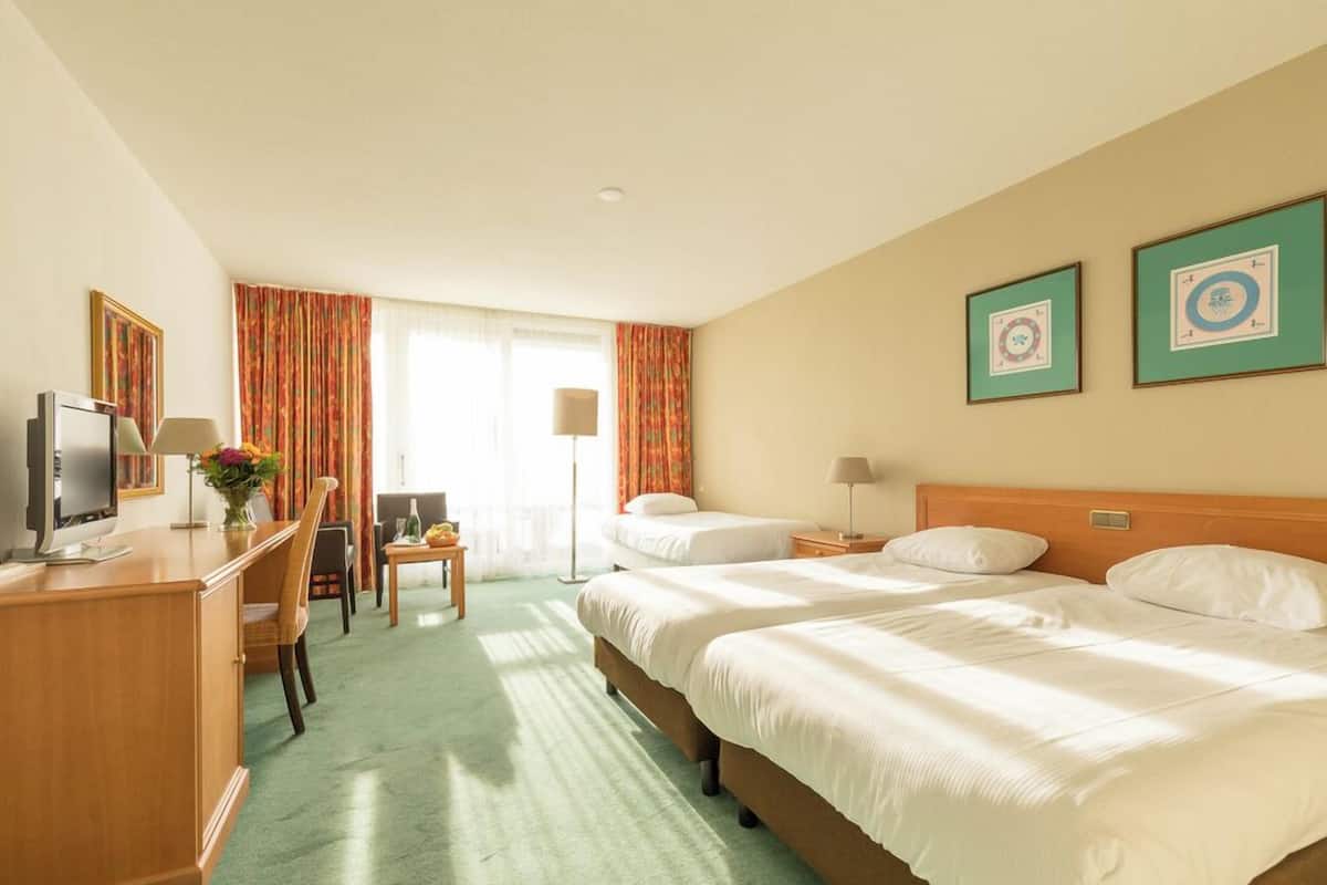 A hotel room with two beds, a desk with a computer, a chair, a lamp, and a window with curtains.
