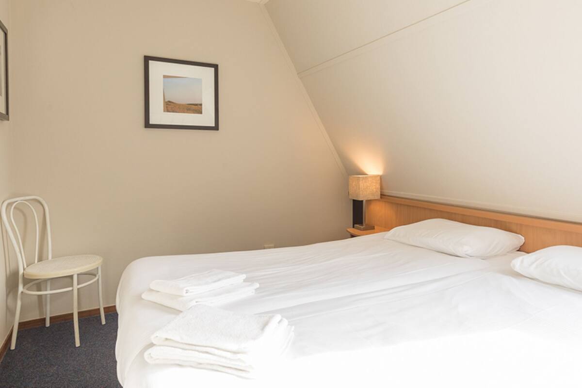 Ein Hotelzimmer mit einem Bett, einem Sessel, einer Lampe und einem gerahmten Bild an der Wand.