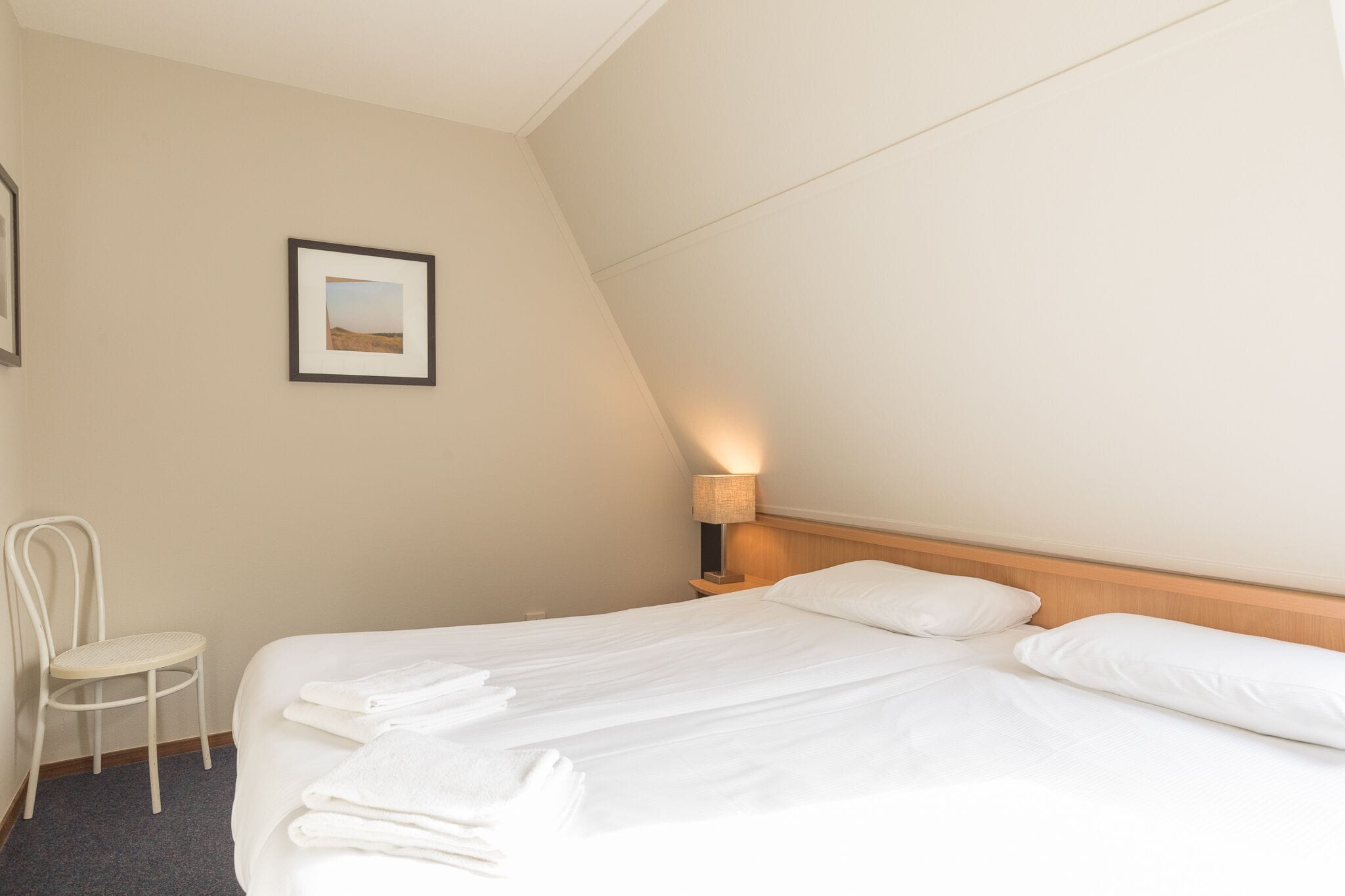 A hotel room with a bed, a chair, a nightstand with a lamp, and a framed picture on the wall.