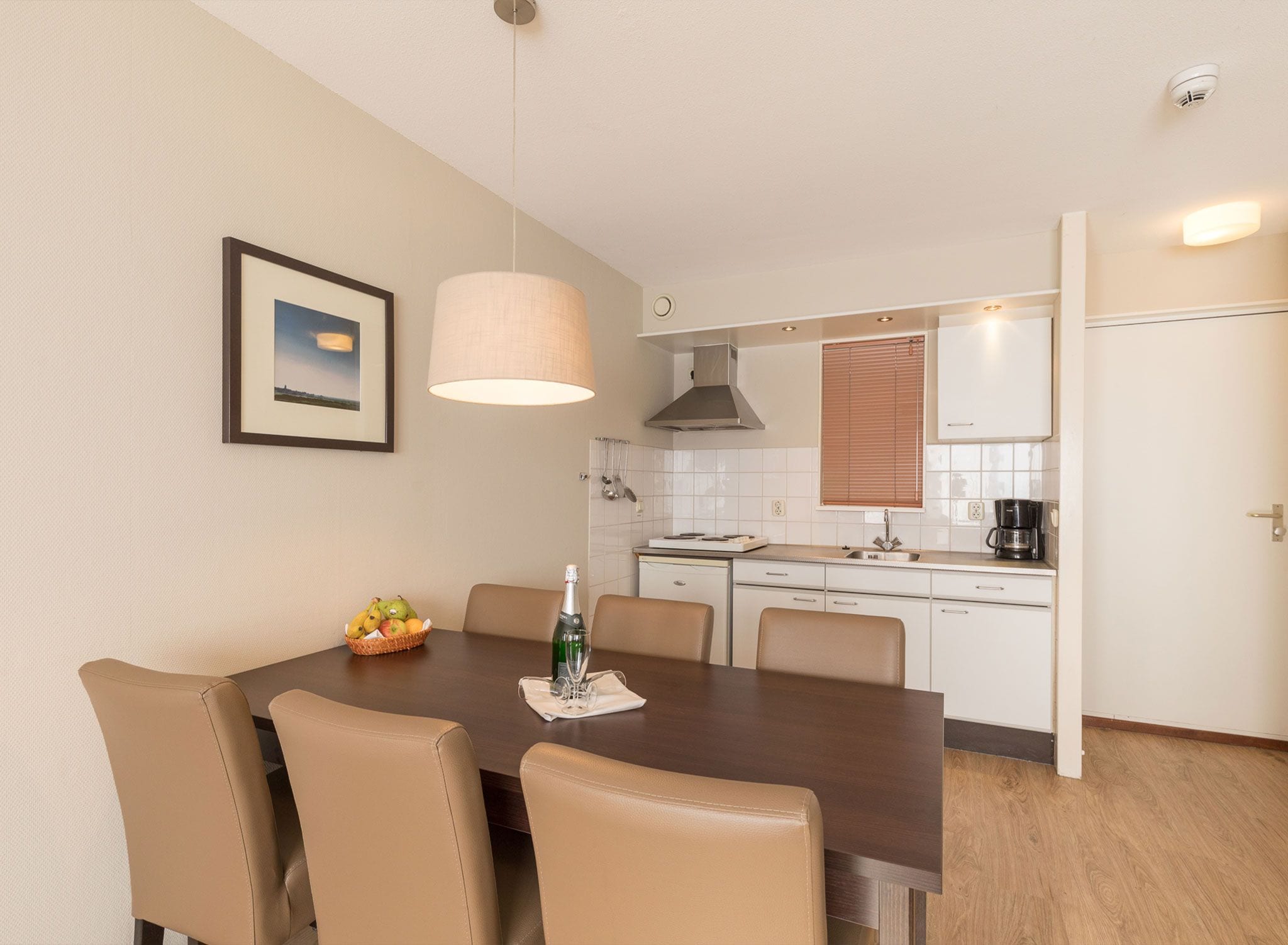 A modern kitchen with white cabinets, a dining table with chairs, a hanging light fixture, and a framed picture on the wall.