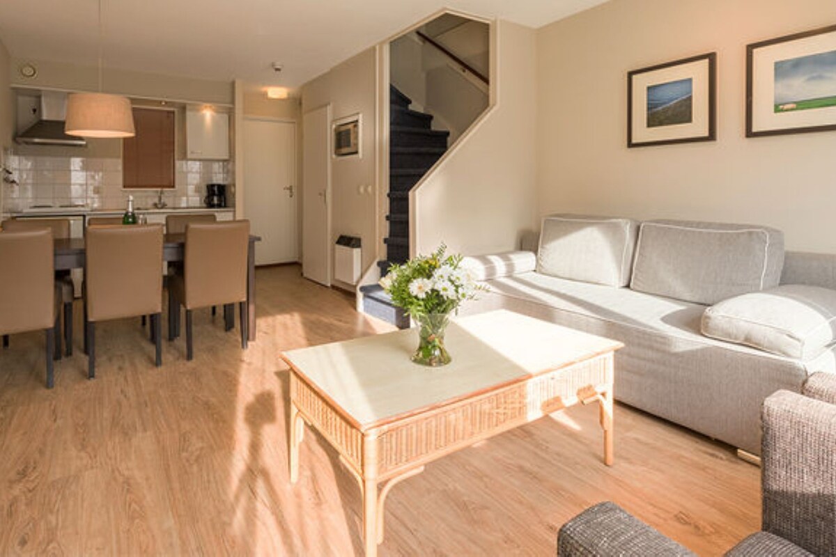 Una sala de estar moderna con un sofá, una zona de comedor con sillas, una cocina con estufa y una escalera.