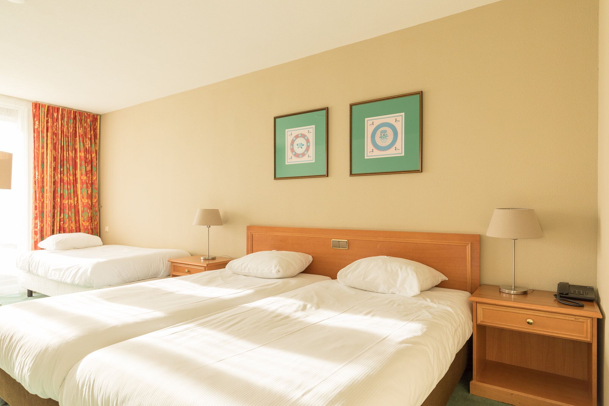 Ein Hotelzimmer mit zwei Betten, einem Holzkopfteil, Nachttischen mit Lampen und zwei gerahmten Bildern an der Wand.