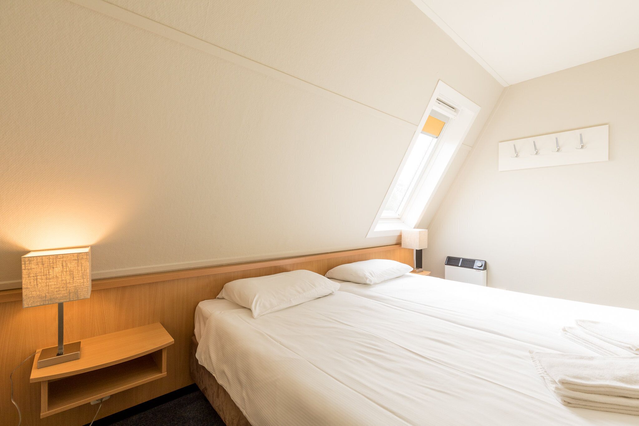 Une chambre d’hôtel comprenant un lit, des lampes de chevet, une petite étagère, une fenêtre et un climatiseur fixé au mur.