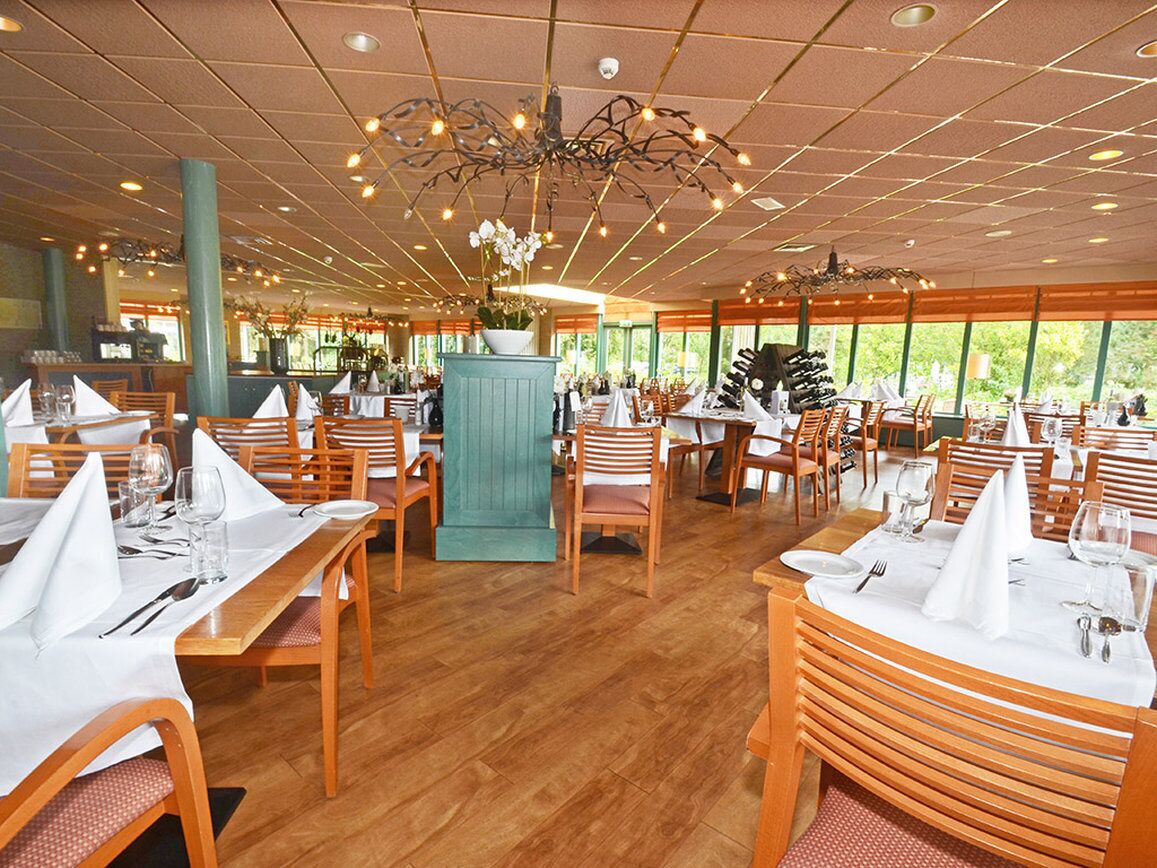 A restaurant with wooden tables and chairs, a central decorative column, and large windows.