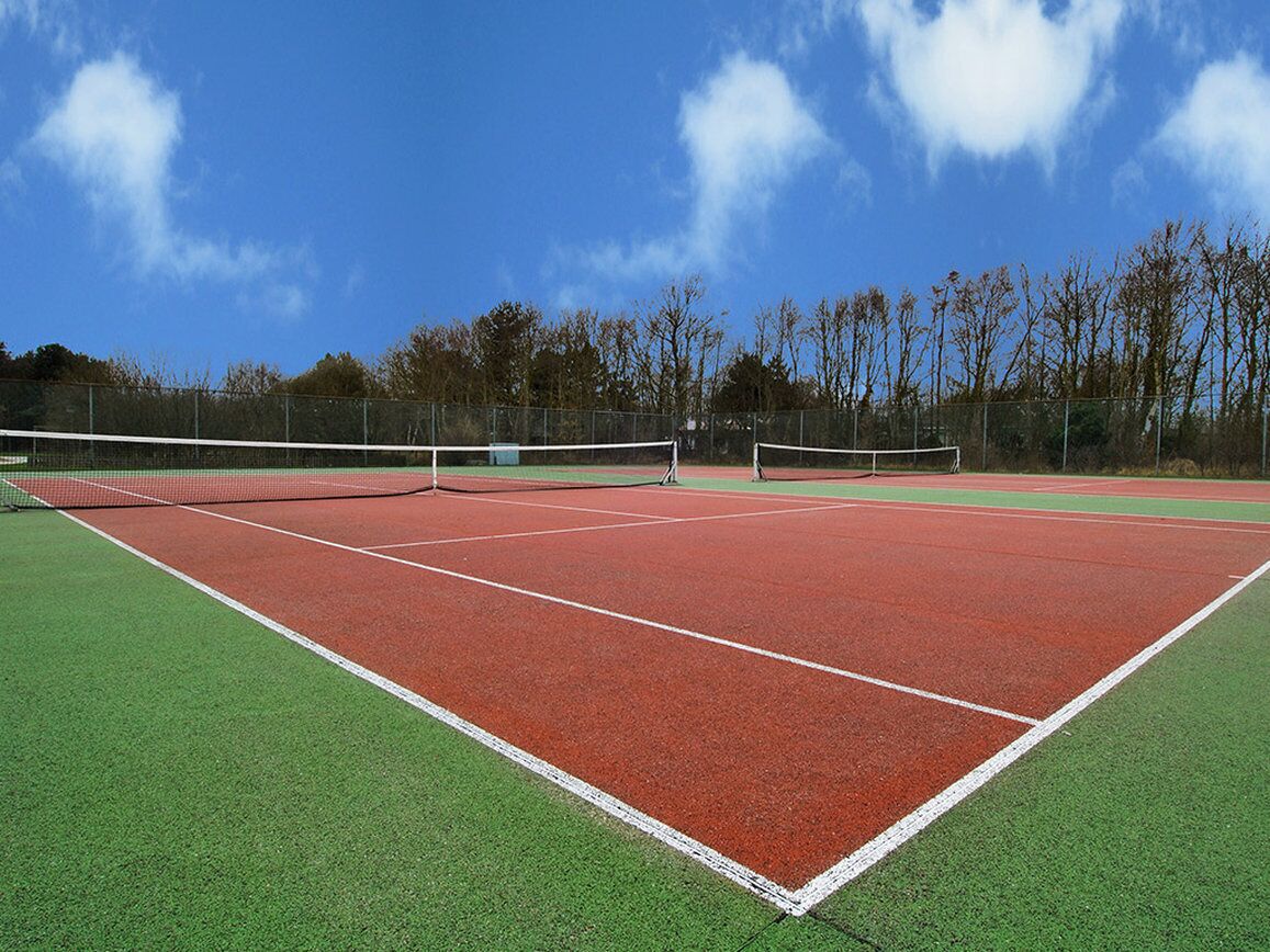 A tennis court with a net, surrounded by a green field and trees.