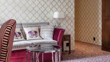 Una habitación con papel tapiz estampado, un armario de madera, un sofá con cojines a rayas, una mesita redonda pequeña y dos lámparas de pie.
