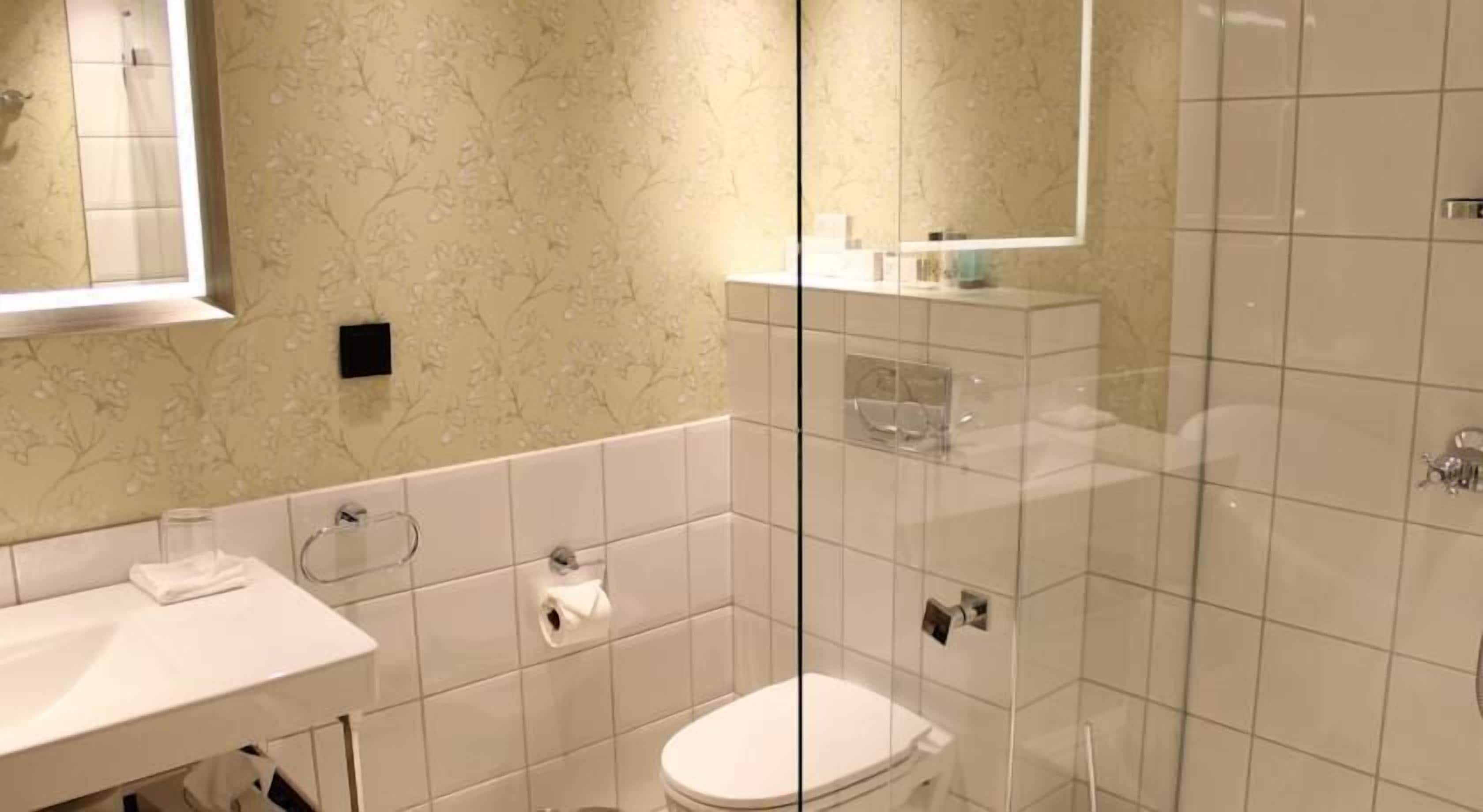 Moderni kylpyhuone, jossa on valkoinen pesuallas, wc ja suihkutila.
