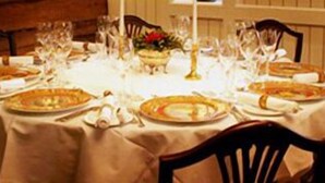 Mesa de jantar redonda posta para uma refeição, com pratos, talheres e copos.