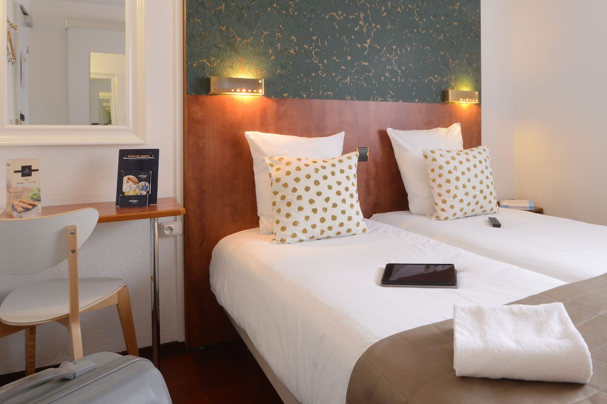 A hotel room with two beds, a desk, a chair, and a suitcase.