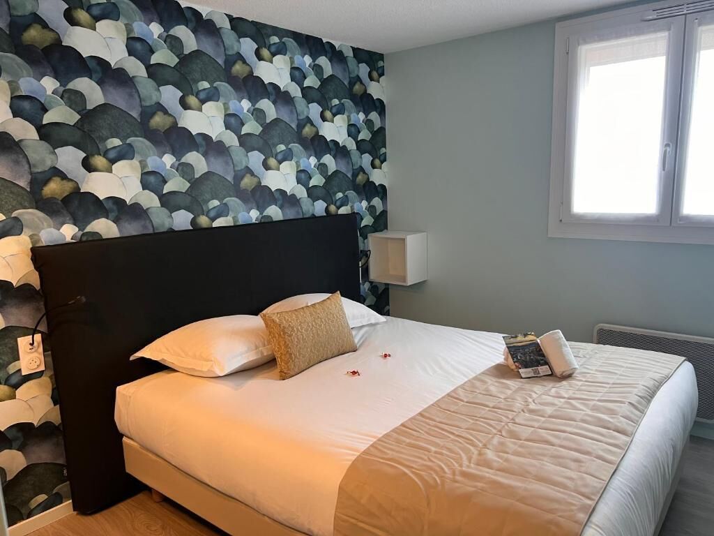 A neatly made bed with a white comforter and pillows, a dark headboard, and a wall with a textured pattern.