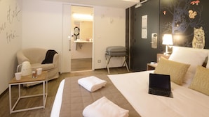 A hotel room with a bed, a laptop, a chair, a small table with a kettle and cups, and a bathroom visible through an open door. - Arc-En-Ciel Colmar (Colmar)