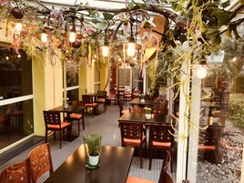 Un comedor interior con mesas y sillas, plantas colgantes e iluminación colgante.